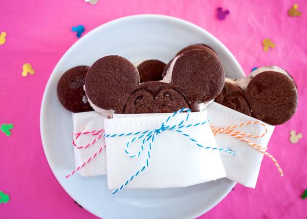 Mickey Mouse shaped ice cream sandwiches wrapped in paper with colorful twine. 