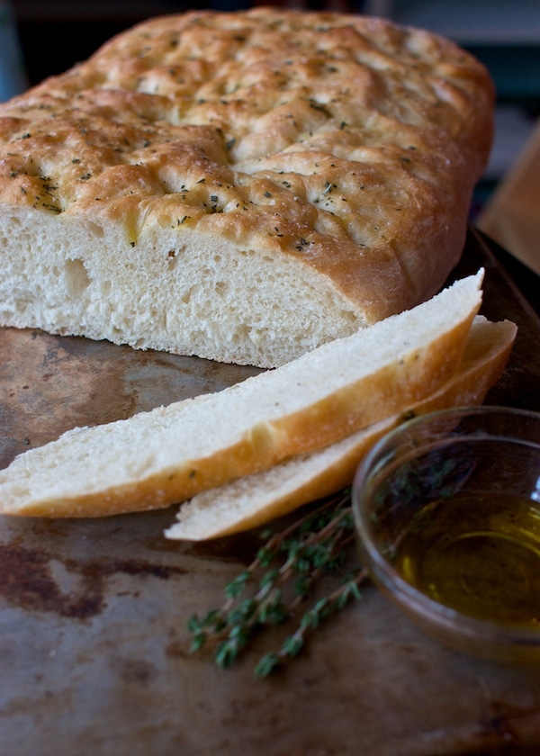 A loaf of fresh focaccia cut into slices with oil and herbs. 