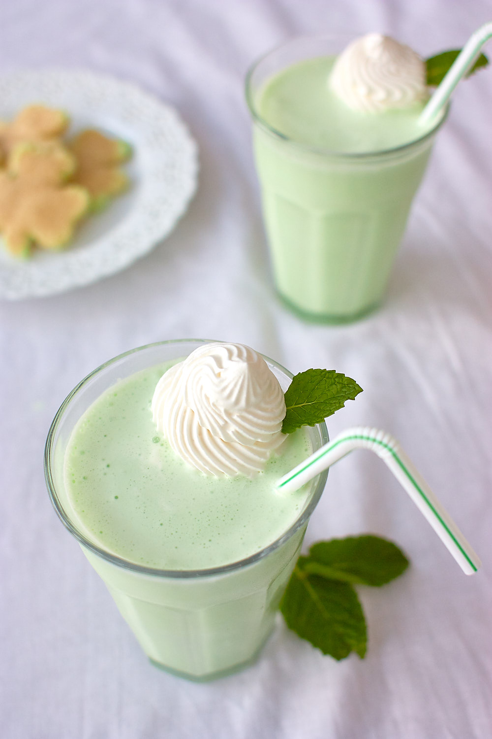 Green mint shakes on a table with mint and shamrock shaped cookies. 