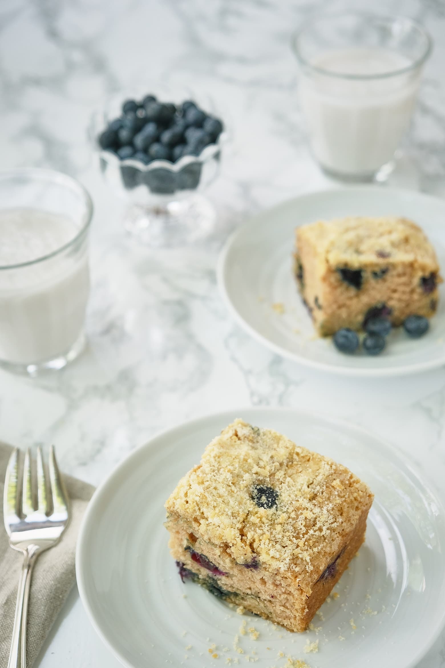 Two pieces  of blueberry boy bait crumbcake on a plate with a fork. 