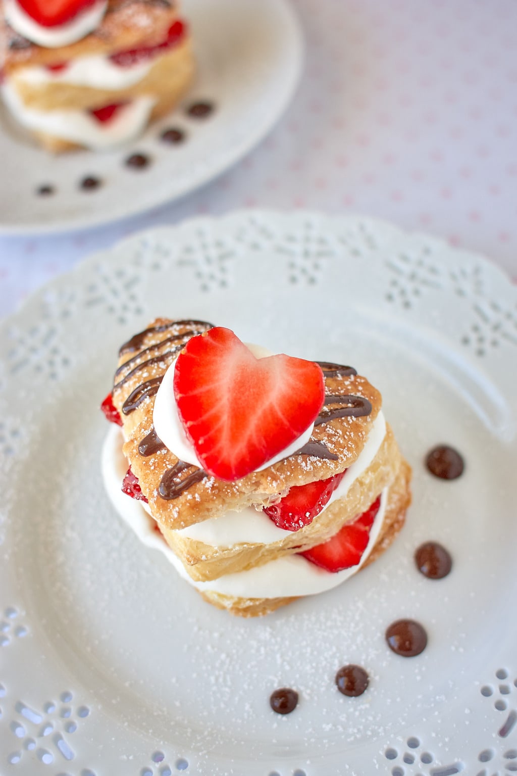Heart shaped strawberry napoleon dessert with chocolate sauce, strawberries, and whipped cream on a plate. 