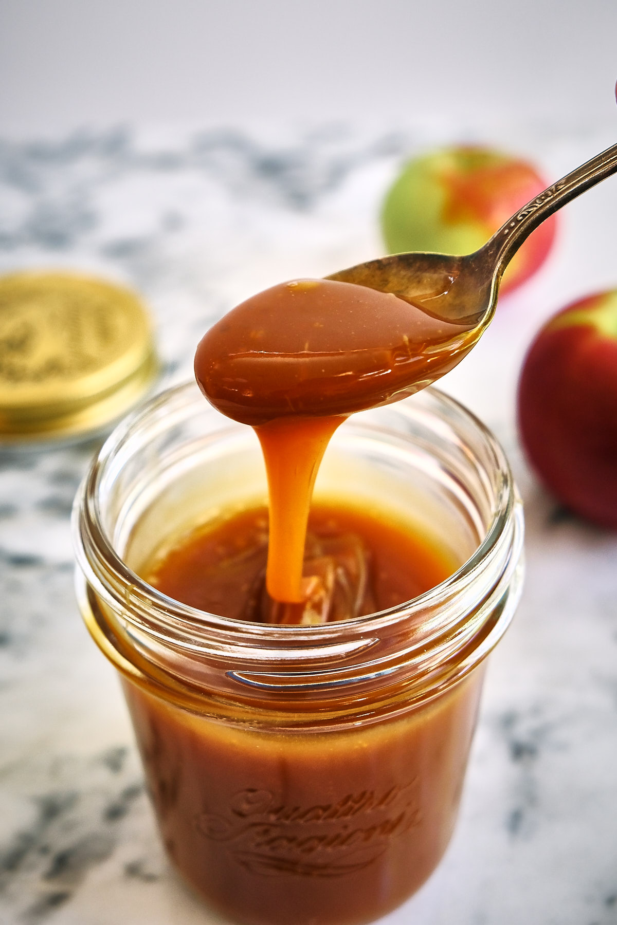 A spoonful of dairy free caramel apple dip from a mason jar with apples on the table. 