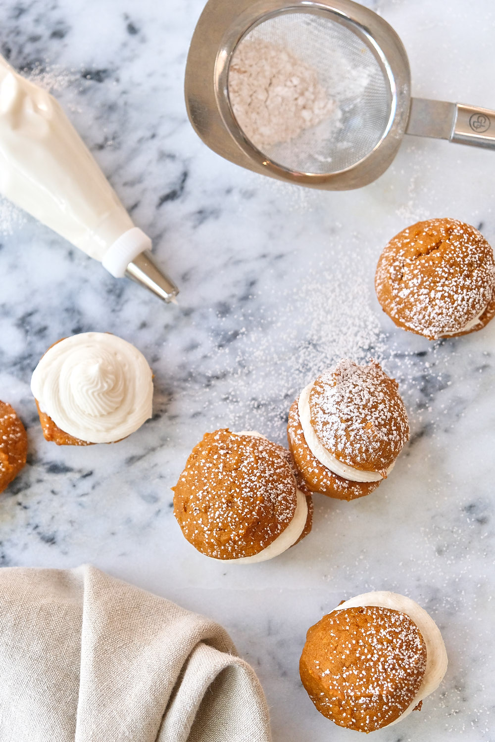 Mini pumpkin whoopie pies on table with a dusting of spices and powdered sugar. 