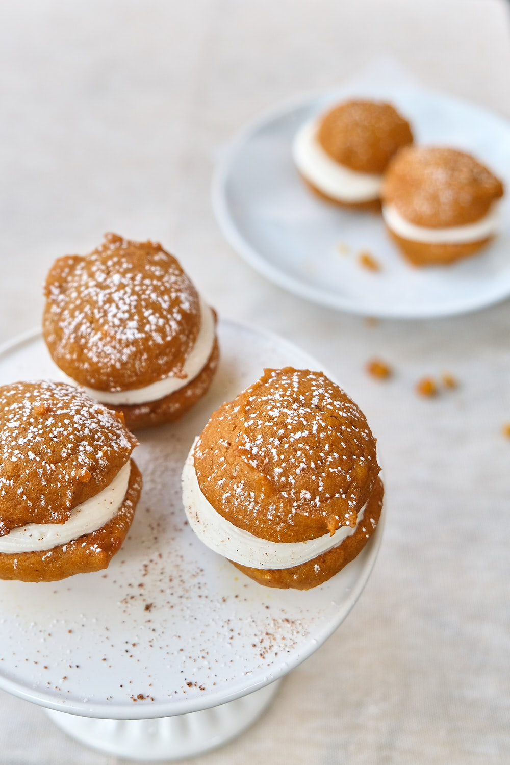 Mini pumpkin whoopie pies on a cake stand with a dusting of spices and powdered sugar. 