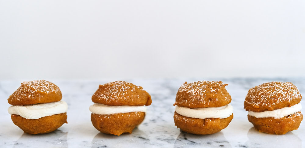 A row of four pumpkin whoopie pies on a marble countertop. 