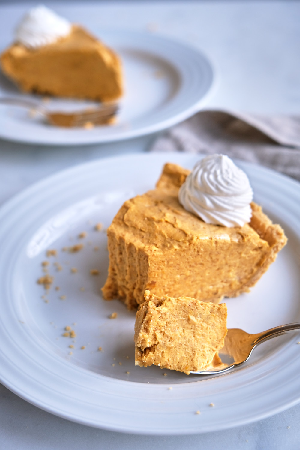 A slice of pumpkin cream pie on a plate with a bite on a fork. 