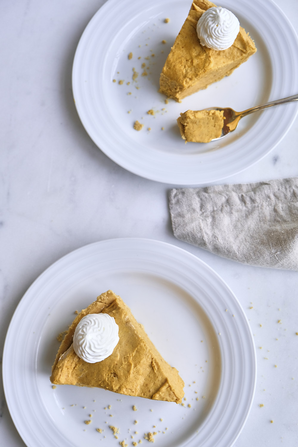 Two slices of pumpkin cream pie on plates with whipped cream.