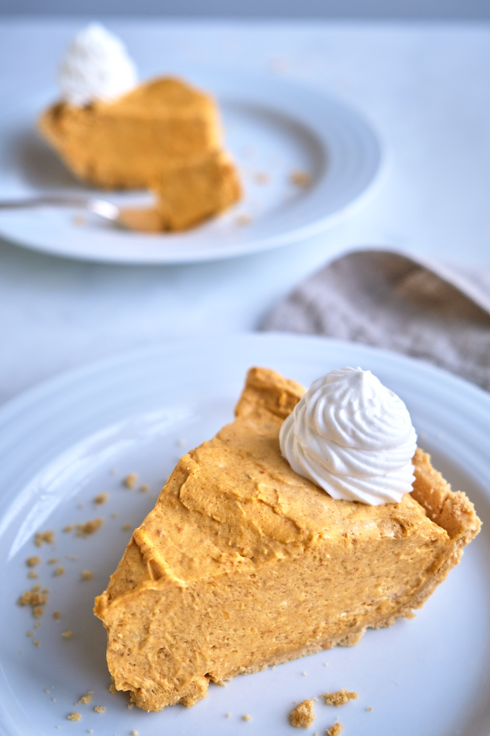 A slice of pumpkin cream pie on a plate with whipped cream. 