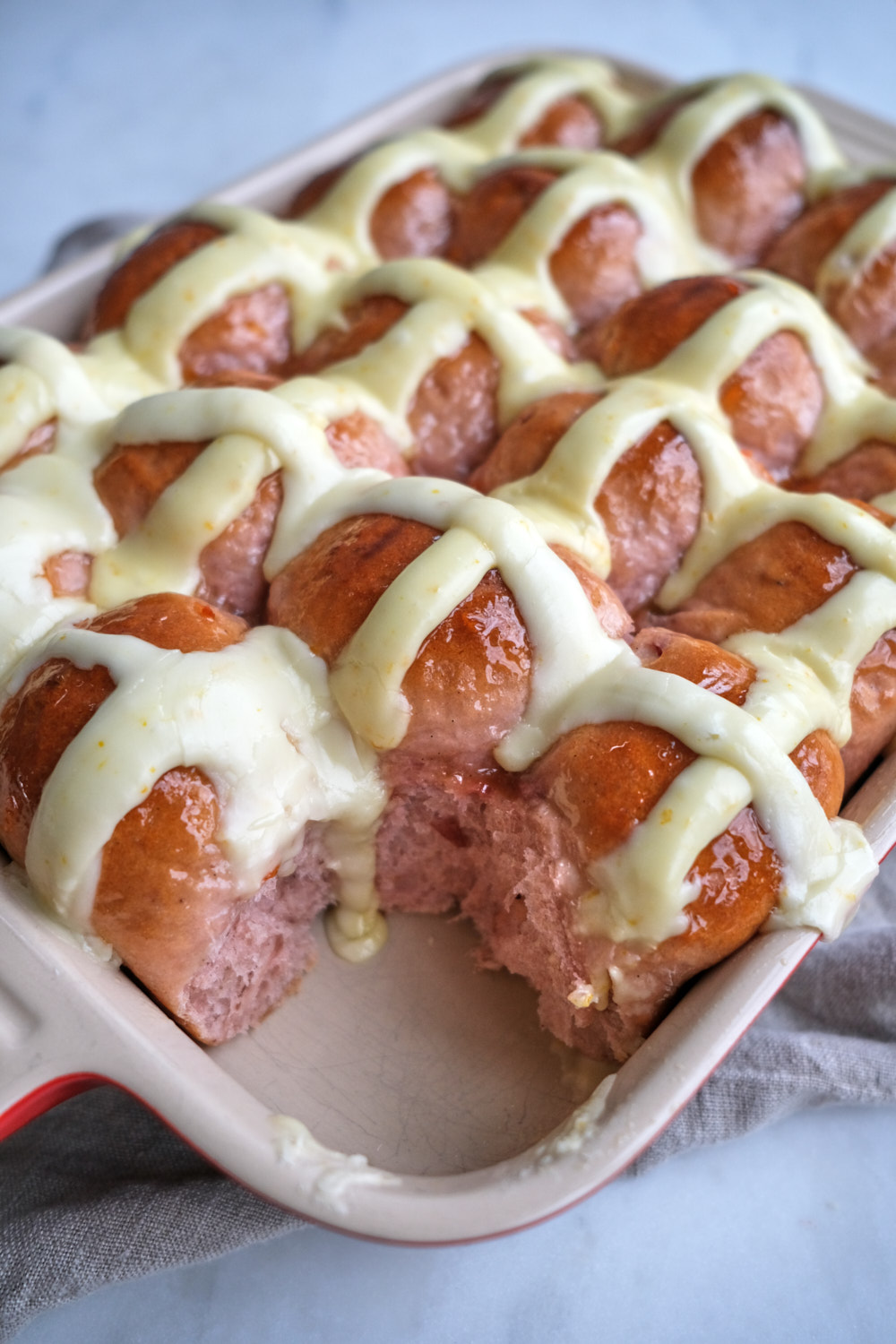 A pan of hot cross buns, one is missing from the corner of the pan. 