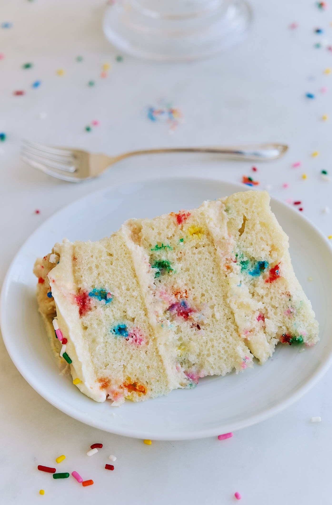 A slice of dairy-free egg-free Milk Bar Birthday Cake on a plate with a fork. 