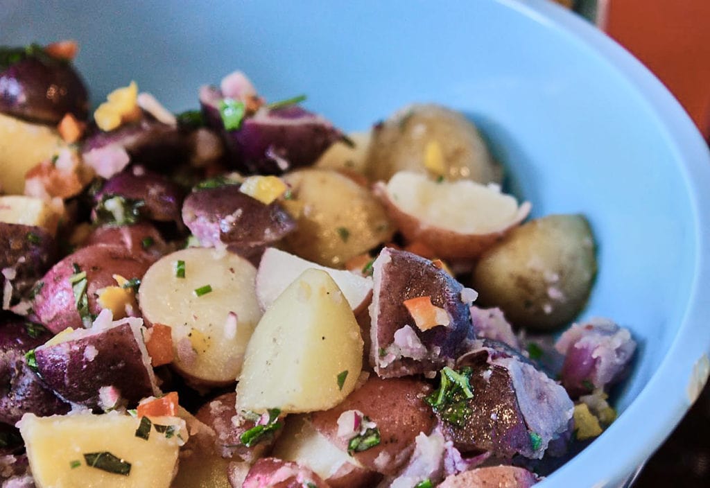 A dairy-free potato salad with multi-colored potatoes and herbs in a blue bowl. 