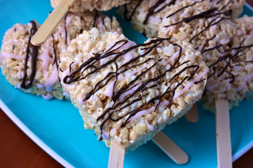 Heart shaped rice krispies treats with chocolate and pink frosting drizzle.