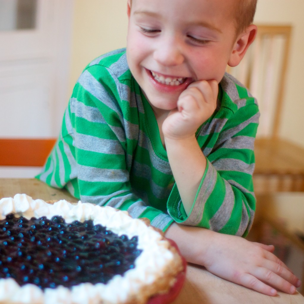 A cute kid looking at a fresh blueberry pie.