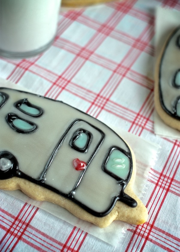 A camper sugar cookie on a gingham tablecloth with a glass of milk
