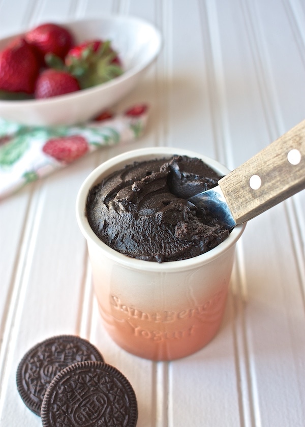 A container of chocolate oreo spread in a jar with strawberries