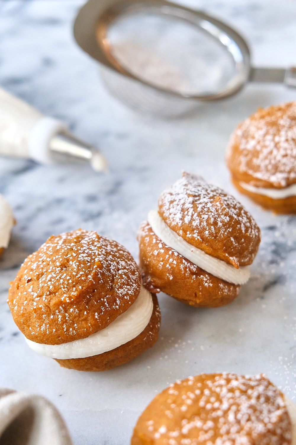 Two mini pumpkin whoopie pies on a table with a dusting of spices and powdered sugar. 