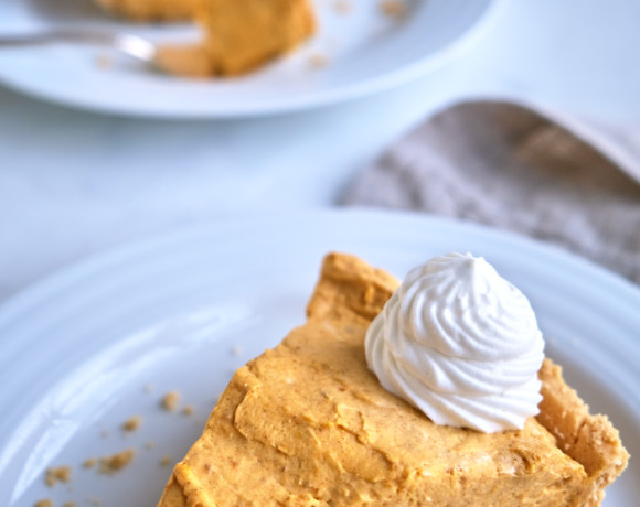 A slice of pumpkin cream pie on a plate with whipped cream.